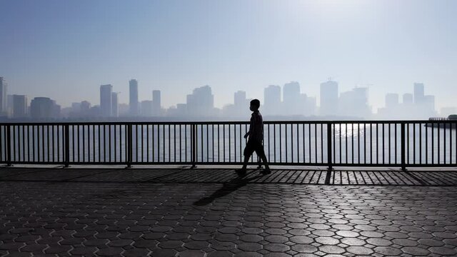 Silhouettes of a 10-year-old boy having his morning walk in a foggy morning at Khalid Lake in Sharjah, United Arab Emirates, 4K Video