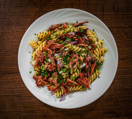 pasta fusilli salad with tuna and onion in white plate on a wooden background. with copy space. top view