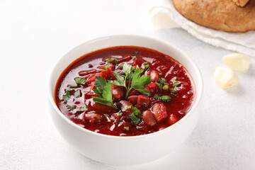 Russian and Ukrainian cuisine. Borscht with beans in a white bowl. Garlic and tortillas on a white table. Beetroot, bean, potato soup with parsley. Background image, copy space