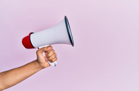 Hand of hispanic man holding megaphone over isolated pink background.