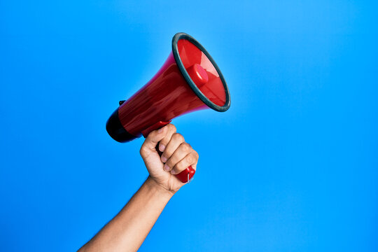 Hand of hispanic man holding megaphone over isolated blue background.