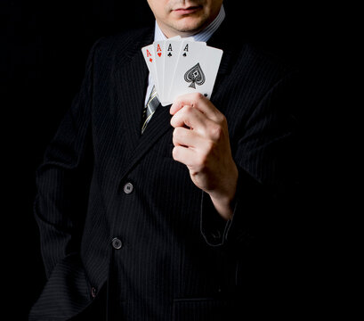 A man in a black suit and a tie holds 4 aces in his hand with black background. Poker cards. Play in poker and gambling games. Use for gambling sites, articles, advertising, gifts.  close up