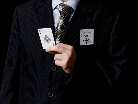 A man in a black suit and a tie holds 1 black ace in his hand with black background, in pocket joker card. Poker cards. Play in poker and gambling games. Use for gambling sites, articles, advertising