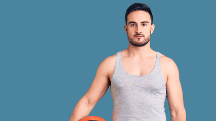 Young handsome man holding basketball ball thinking attitude and sober expression looking self confident