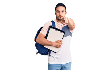 Young handsome man wearing student backpack and notebook pointing with finger to the camera and to you, confident gesture looking serious