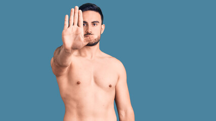Young handsome man wearing swimwear doing stop sing with palm of the hand. warning expression with...
