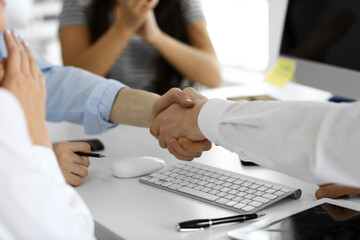 Two businessmen are shaking hands in office while sitting at the desk, close-up. Colleagues applauding of success meeting end. Business people concept