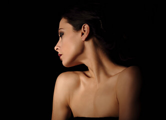 Beautiful mysterious woman in darkness with healthy neck and golden health skin in shadows on dramatic  black background with empty copy space. Closeup