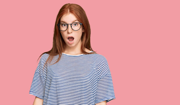 Young read head woman wearing casual clothes and glasses afraid and shocked with surprise and amazed expression, fear and excited face.