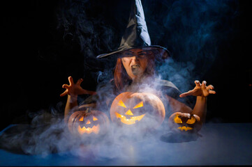 The evil witch casts a spell on pumpkins. Portrait of a woman in a carnival halloween costume in the dark