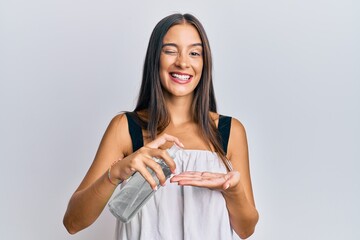 Young hispanic woman using hand sanitizer gel winking looking at the camera with sexy expression,...