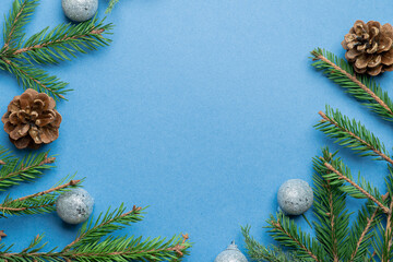 Obraz na płótnie Canvas Fir, spruce branches, pine cones and Christmas tree toys on blue background with copy space