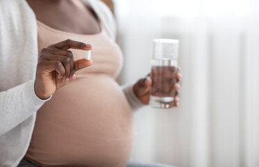 Supplements During Pregnancy. Unrecognizable Black Expectant Lady Holding Pill And Water Glass