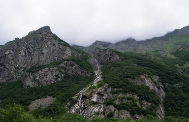 Midagrabindon  waterfalls in the gorge. Mountains in the North Caucasus in summer. Mountain tops in the clouds.
