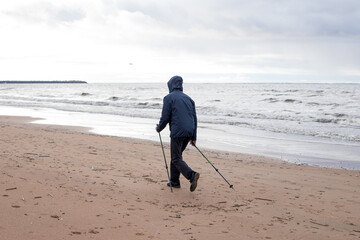 senior nordic pole walker enjoying nice autumn day outdoors, near sea. active elderly man and woman wearing sport clothes having walk by lake using specially designed poles. Selective focus