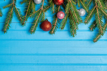 Fototapeta na wymiar Fir, spruce branches and Christmas tree toys on blue wooden background with copy space