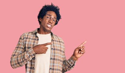 Handsome african american man with afro hair wearing casual clothes and glasses pointing aside worried and nervous with both hands, concerned and surprised expression