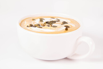 Pumpkin soup decorated with cream and pumpkin seeds in a bowl on a white background