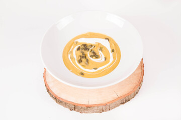 Pumpkin soup decorated with cream and pumpkin seeds on a plate on a piece of wood