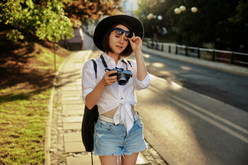Fototapeta premium The girl in the black hat and sun glasses with photo camera on a road in an old european town.