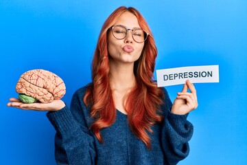 Young redhead woman holding brain and depression text looking at the camera blowing a kiss being...