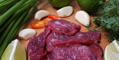 Raw beef sliced on a board with fresh vegetables