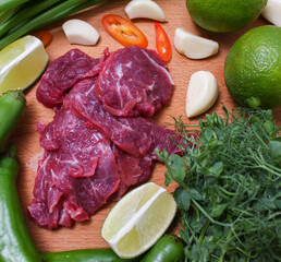 Raw beef sliced on a board with fresh vegetables