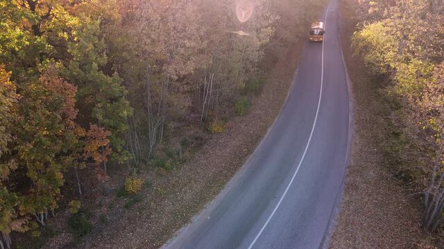 Aerial view of road with school bus in beautiful autumn forest at sunset.