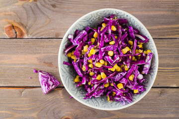 Fototapeta na wymiar Diet snack. Red cabbage salad with corn grains in a plate on a wooden table. Vegetarian food. Top view