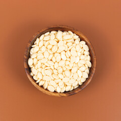 Wooden bowl with natural wax granules on brown background. Top view. Beauty treatment concept