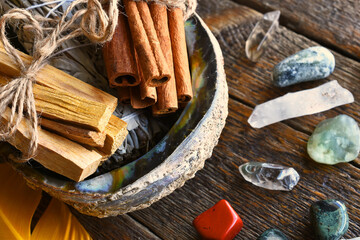 A close up image of smudge kit with a white sage bundle, cinnamon sticks, and palo santo in a abalone shell. 