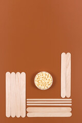 Depilation vertical background. Wooden spatulas and jar with natural granular wax on brown backdrop. The concept waxing.