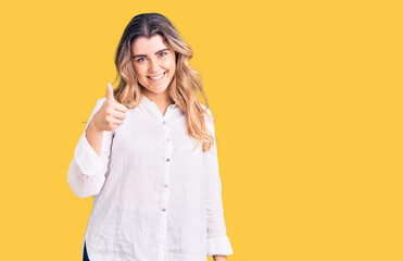 Young caucasian woman wearing casual clothes doing happy thumbs up gesture with hand. approving expression looking at the camera showing success.