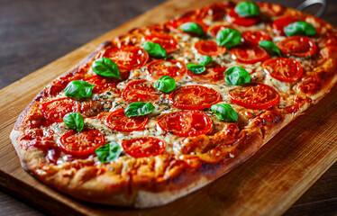 oval Pizza with Mozzarella cheese, Tomatoes, pepper, Spices and Fresh Basil. Italian pizza. Pizza Margherita or Margarita on wooden table background