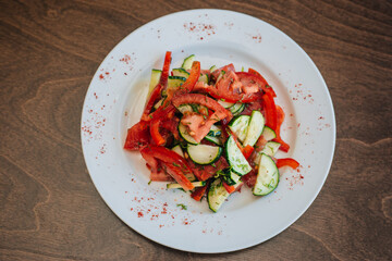 Classic salad with cucumbers and tomatoes sprinkled with dill. Diet food. On a white plate. Dish on a dark background.