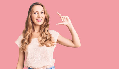 Young beautiful caucasian woman with blond hair wearing casual clothes smiling and confident gesturing with hand doing small size sign with fingers looking and the camera. measure concept.