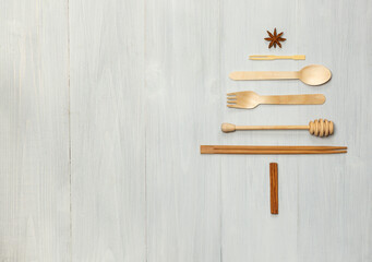 Wooden Forks, knives, spoons and other kitchen accessories laid out in the shape of a Christmas tree on light boards. Horizontally, with space