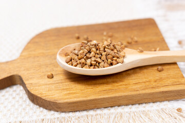 raw buckwheat grain on a wooden spoon on wood table background. selective focus