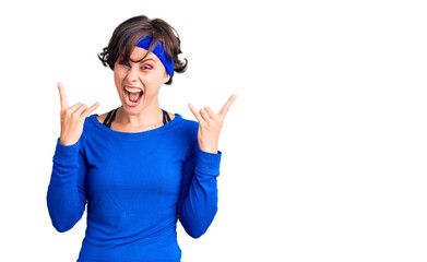 Beautiful young woman with short hair wearing training workout clothes shouting with crazy expression doing rock symbol with hands up. music star. heavy music concept.