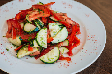 Classic salad with cucumbers and tomatoes sprinkled with dill. Diet food. On a white plate. Dish on a dark background.