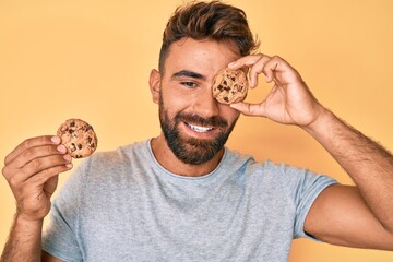 Young hispanic man holding cookie winking looking at the camera with sexy expression, cheerful and...