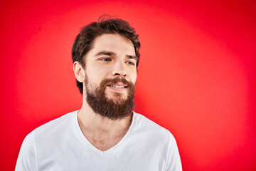 A man in a white T-shirt with a beard gestures with his hands emotions red background