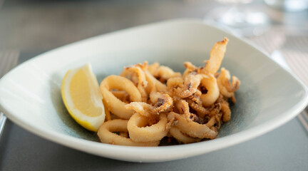 Close up of delicious crispy deep fried calamari with lemon on a white plate.