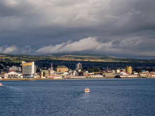 Punta Arenas, Chile - December 12, 2008: Sun shines on Cityscape of coastline at harbor and dark...