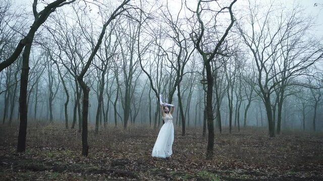 Ghost of the bride walks through the forest in the fog. Scary Halloween costume with bloody blindfold