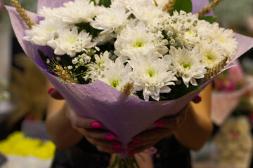 beautiful, bouquet of white chrysanthemums, in women's hands, in a flower shop. The seller, a girl, holds out a bouquet for a holiday. Flower trade, private business, losses, loss of customers