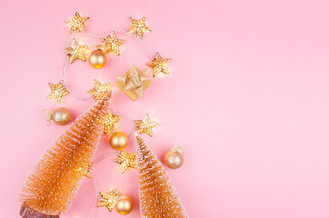 Christmas background in gold glitter color - christmas trees, balls, gift box and glowing stars lights on light pink background, flat lay.