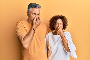 Beautiful middle age couple together wearing casual clothes smelling something stinky and disgusting, intolerable smell, holding breath with fingers on nose. bad smell