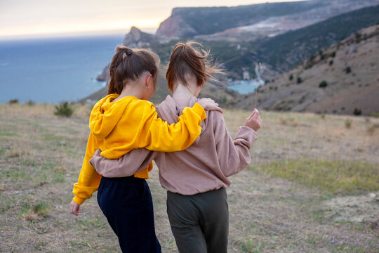 Two preteen girls traveler wearing yellow and biege hoodie walking  on top of the mountain landscape and looking to the sea