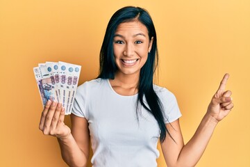 Beautiful hispanic woman holding 500 russian ruble banknotes smiling happy pointing with hand and finger to the side